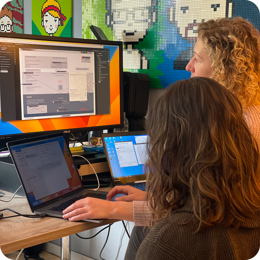 Zwei Mitarbeiterinnen von Gebrüder Pixel sitzen vor einem Bildschirm und machen ein Dokument barrierefrei
