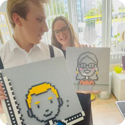 Zwei Mitarbeiter:innen halten Lego-Portraits in die Kamera