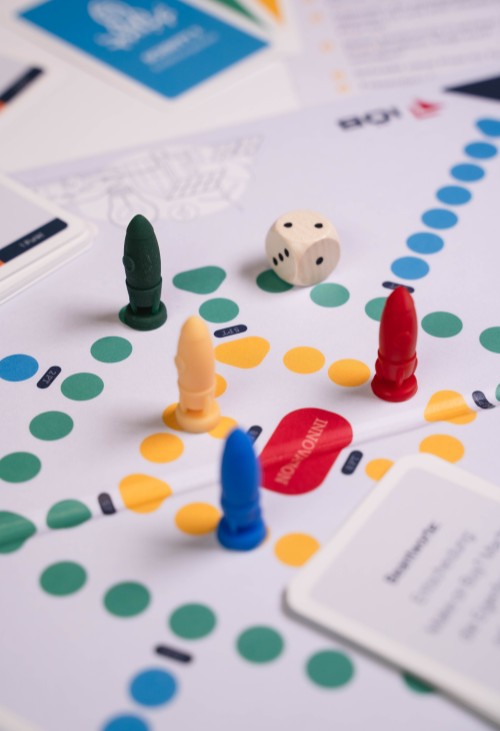 Nahaufnahme des IOEB-Brettspiels mit Spielfiguren, Karten und einem Würfel